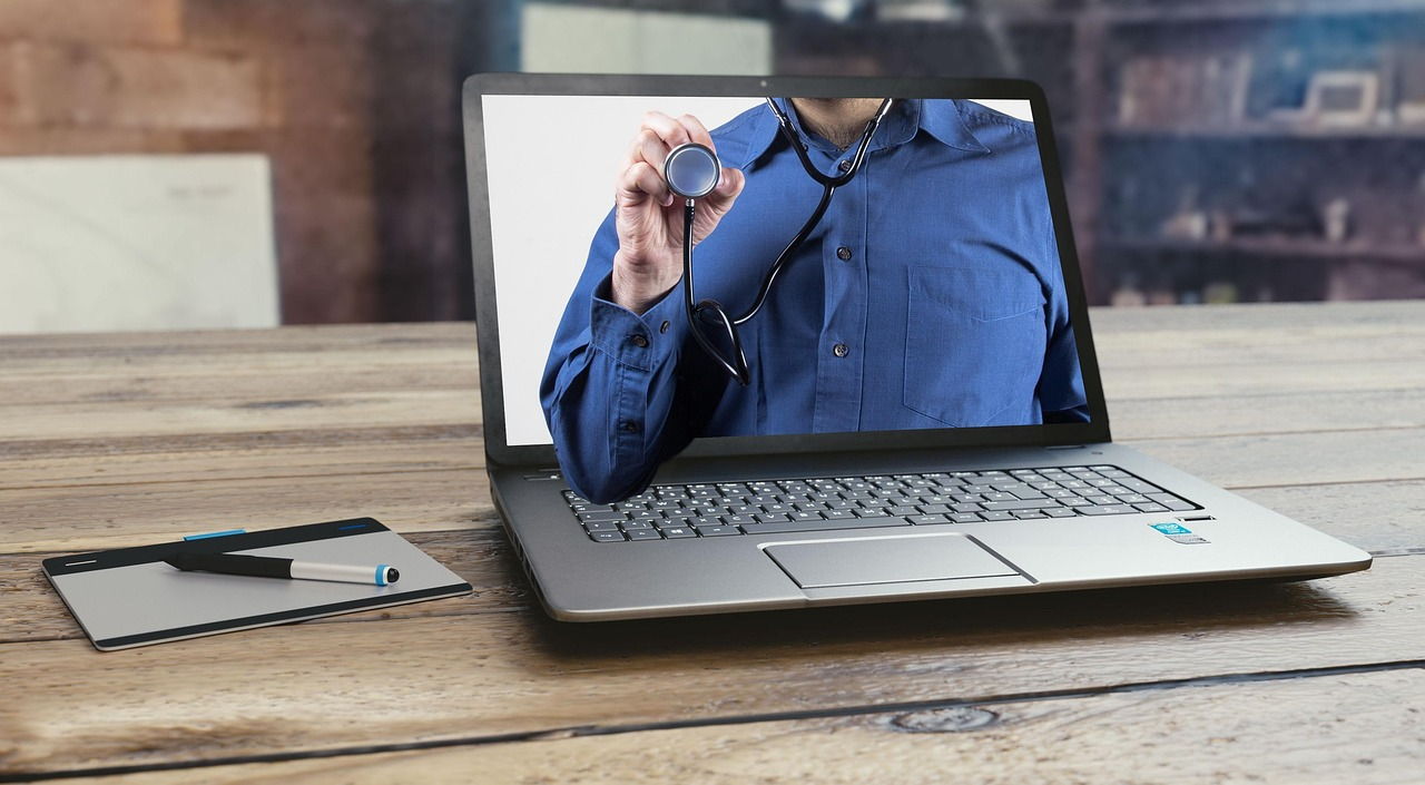 Laptop na drewnianym biurku z lekarzem trzymającym stetoskop na ekranie